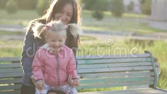 妈妈和小女儿坐在公园的长凳上春天在户外视频的预览图