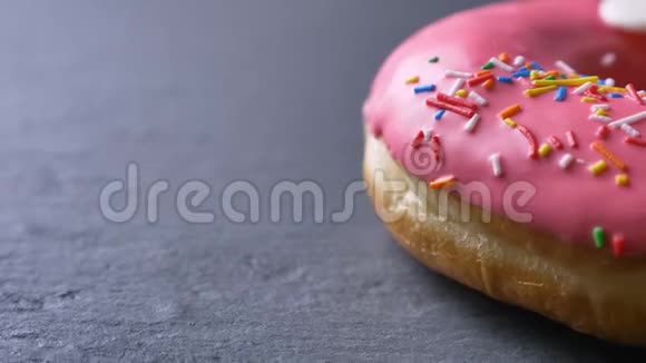 特写半幅美味的粉红色甜甜圈配上五颜六色的薯片眼睛在灰色的桌子背景上慢慢旋转视频的预览图