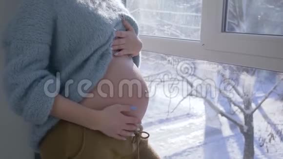 男女双手托着肚子一对夫妇在家中站在大窗户旁抚摸着赤裸的大肚子视频的预览图