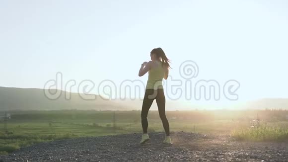 拳击的女孩在日落或日出时在山顶上锻炼她在大自然中锻炼高踢脚女性视频的预览图