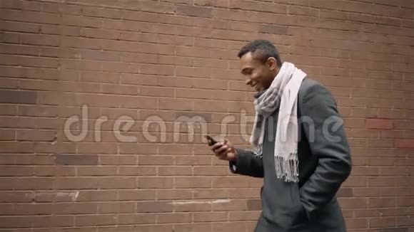 穿着外套和围巾的非裔美国人发短信走路视频的预览图