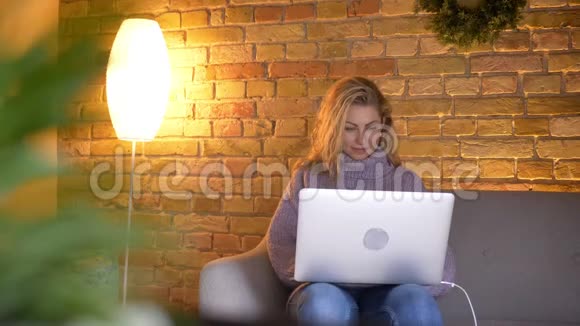 在舒适的室内沙发上坐着的白种人成年女性电脑打字特写镜头视频的预览图