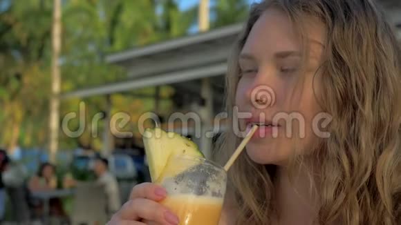 迷人的年轻旅游女孩在海滩度假胜地与美丽的日落一起喝着新鲜的热带皮纳科拉达鸡尾酒视频的预览图