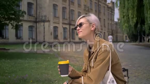 金发时尚的女士戴着太阳镜短发喝着咖啡看着相机微笑着视频的预览图