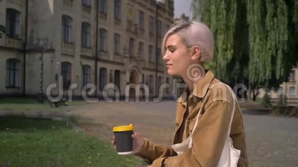 时尚金发女人短发喝咖啡坐在大楼附近放松视频的预览图