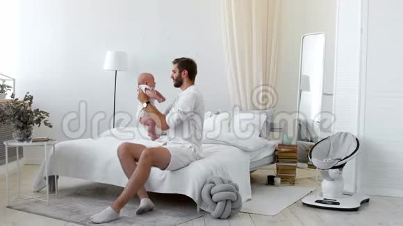 爸爸和宝宝坐在一起在家里的床上看书背景是白色的视频的预览图