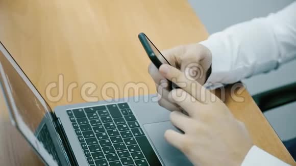 一个商人的手在办公室里用电话和笔记本电脑工作特写镜头视频的预览图