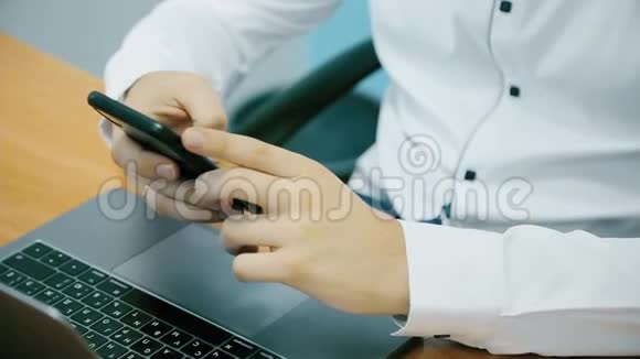 一个商人的手在办公室里用电话和笔记本电脑工作特写镜头视频的预览图