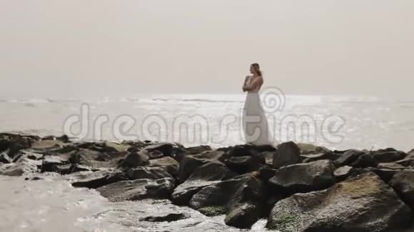 美丽的白衣少女站在石岸望着大海视频的预览图