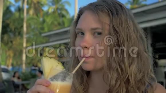 迷人的年轻旅游女孩在海滩度假胜地与美丽的日落一起喝着新鲜的热带皮纳科拉达鸡尾酒视频的预览图