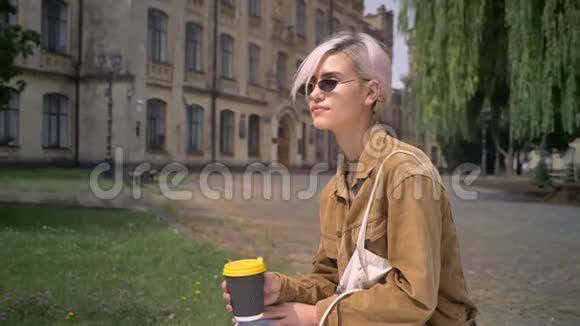 穿着墨镜粉色头发喝着咖啡坐在大学附近的时髦女人视频的预览图
