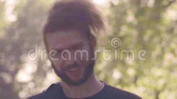 在阳光明媚的公园里一个留着胡须的年轻人在镜头里看着直着凌乱的头发4K前景慢视频的预览图