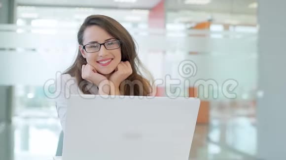 那个女孩在一间宽敞明亮的办公室里在一张带笔记本电脑的桌子上他看着相机微笑视频的预览图