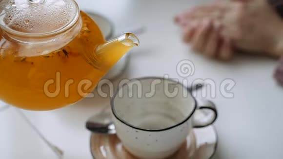 橙色的沙棘茶在茶壶里倒入一个杯子上用女人的手视频的预览图