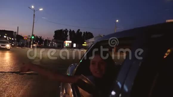 年轻漂亮的女孩骑着一辆车双手伸出窗外在一个深夜的城市里笑慢动作视频的预览图