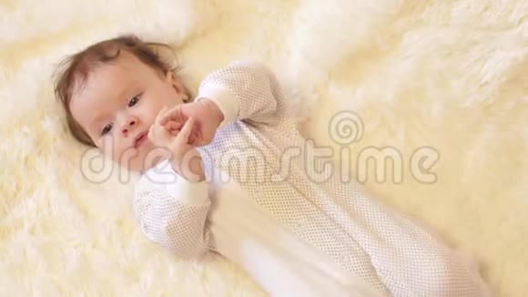 婴儿揉着眼睛躺在他的背上在白色的毯子上视频的预览图
