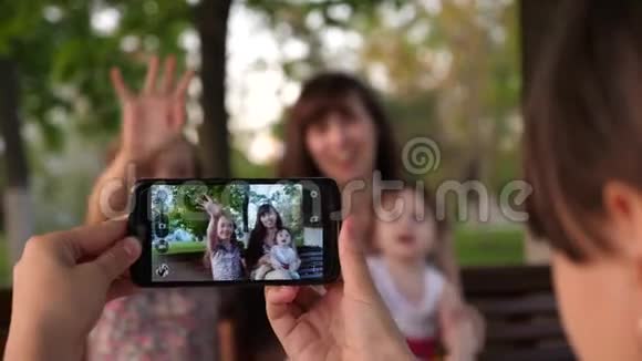 女孩给快乐的年轻母亲拍照孩子们坐在长凳上挥舞着她的手视频的预览图