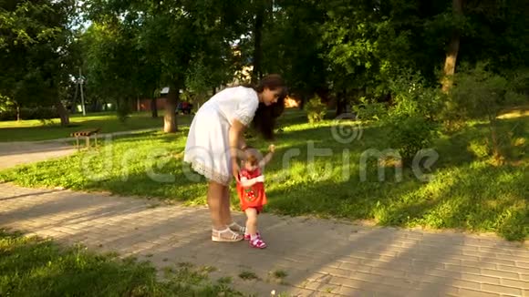 小女孩和她的母亲在公园里学着走小路慢动作视频的预览图