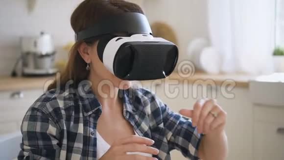 女人用虚拟现实眼镜玩得很开心动动手坐在厨房里视频的预览图