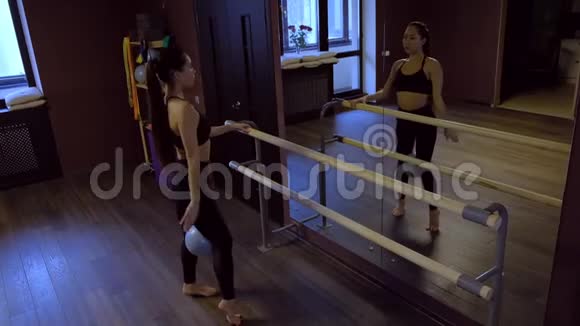 在黑暗房间里的镜子前的芭蕾舞机上身着黑色顶级列车的长马尾辫的苗条女孩慢动作视频的预览图