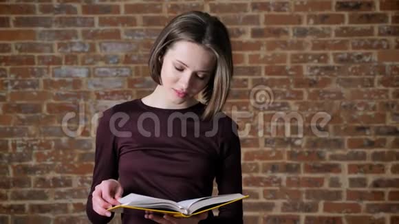 年轻漂亮的女孩正在看书看镜头微笑调情的概念砖背景视频的预览图