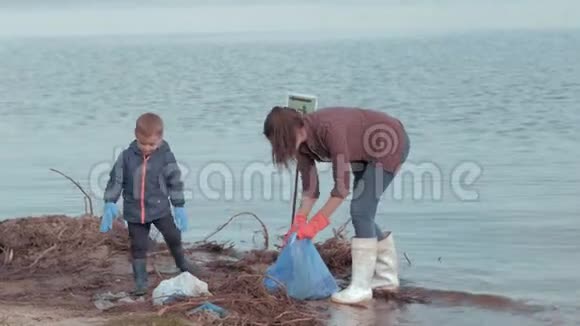停止污染女志愿者带着小男孩从河边的塑料垃圾中清理肮脏的海岸视频的预览图