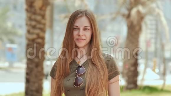 夏日里一个年轻而微笑的女孩在棕榈树的背景下的肖像视频的预览图