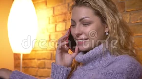 成年白种人金发女性的特写镜头她坐在沙发上随意地在电话上交谈视频的预览图