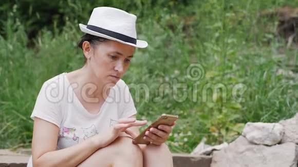 一个戴着白帽子的女人正在智能手机上输入一条信息女孩坐在台阶上拨短信视频的预览图
