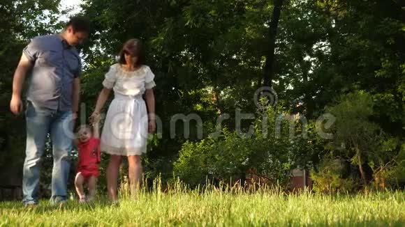 小爸爸妈妈牵着手在城市公园草坪上玩耍慢动作视频的预览图