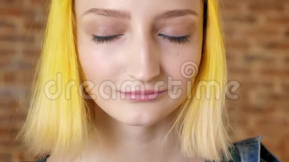 黄色头发的年轻女子的肖像睁开了眼睛砖墙背景模特闭着不寻常的发型视频的预览图