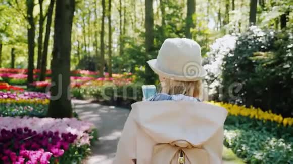 一个手里拿着智能手机的女人漫步在荷兰的基肯霍夫公园视频的预览图