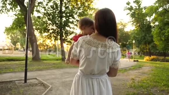 小孩子在夏天坐在妈妈的怀里在公园里散步时揉眼睛慢动作视频的预览图