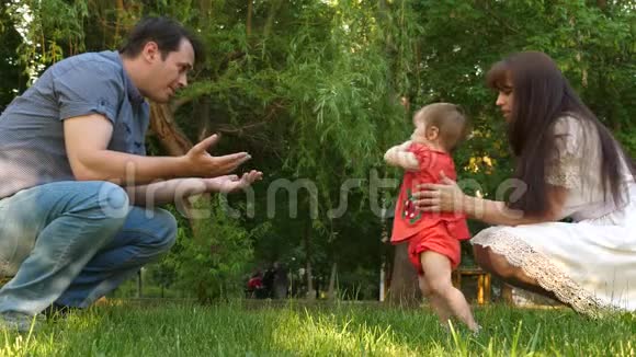 小宝贝迈着第一步在城市公园的草坪草地上和笑得开心的父母玩耍慢动作视频的预览图