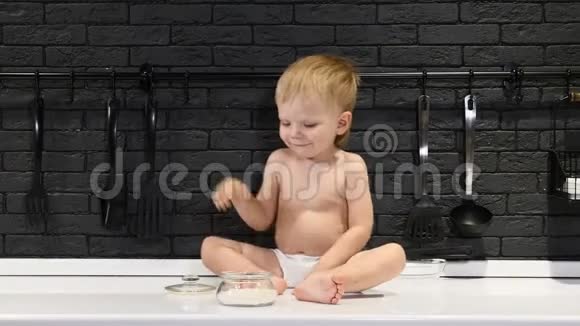 可爱的小男孩坐在厨房的桌子上触摸和品尝糖和吃它玩得开心开心微笑视频的预览图