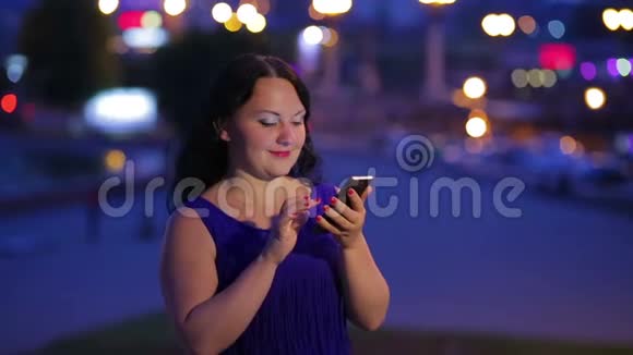 一位穿着蓝色连衣裙的年轻女子拨通电话号码并在智能手机上交谈背景是路灯了视频的预览图