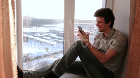 男人用手机在网上看东西坐在窗台上笑视频的预览图