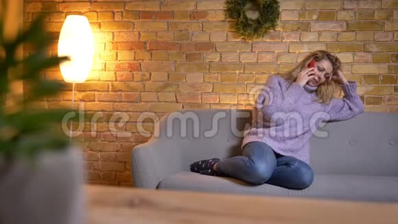 成年白种人金发女性坐在沙发上随意在电话中交谈的特写镜头视频的预览图