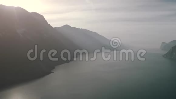意大利朦胧的一天在加尔达湖岸边鸟瞰背光山脉视频的预览图