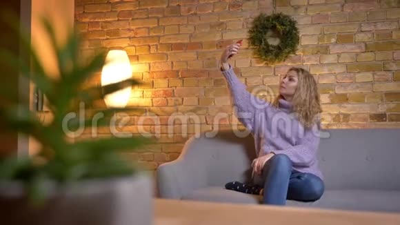 室内舒适的沙发上成年白人金发女在电话里自拍的特写镜头视频的预览图