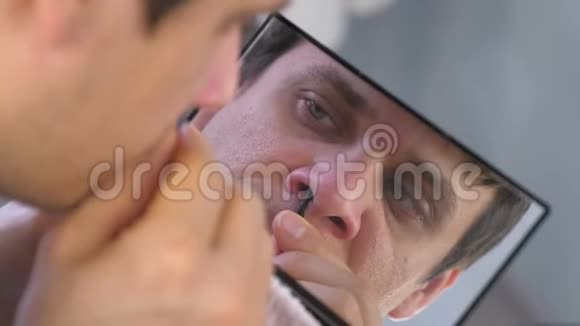 年轻人在家里对着镜子用镊子从鼻子里拔头发视频的预览图