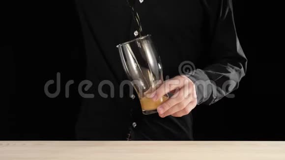 新鲜啤酒手把一瓶美味的手工啤酒从瓶子里倒进黑底木桌里视频的预览图