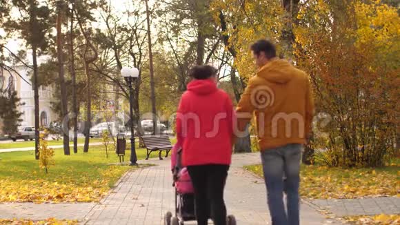 年轻的父母在公园里谈笑风生地拿着小婴儿车在自己面前翻滚视频的预览图