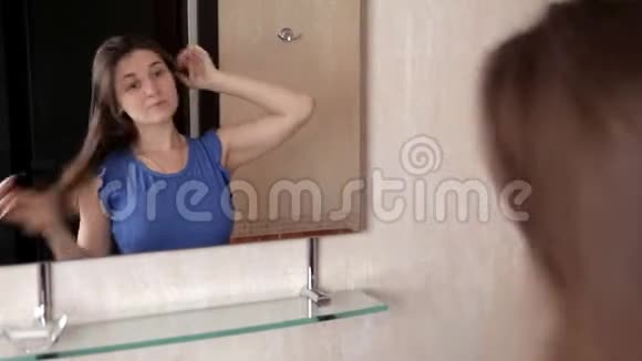 一个年轻的女孩站在镜子前用尾巴把头发梳开视频的预览图