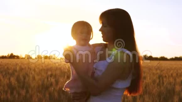 快乐的母亲带着年幼的孩子跳舞笑在金色的夕阳在麦田里慢动作视频的预览图