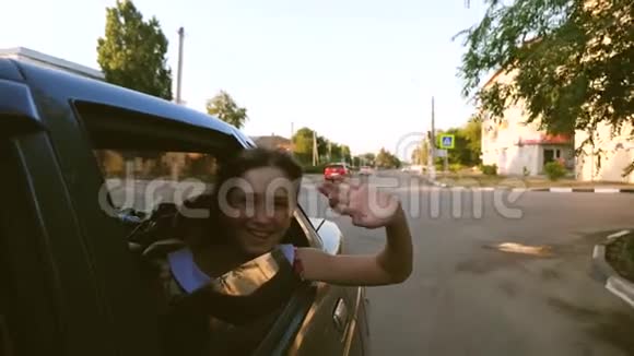 留着长发的漂亮女孩骑着一辆车双手伸出窗外微笑着在市中心挥手慢慢视频的预览图