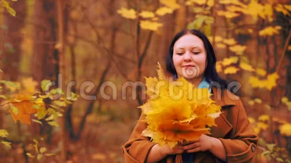 秋天公园里一个年轻的微笑的黑发女人手里拿着枫叶视频的预览图