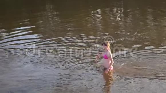 穿着粉红色泳衣的漂亮女孩迎着水流笑着走着女孩正在享受海滩视频的预览图