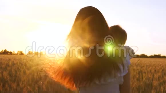 年轻的母亲带着一个小婴儿在麦田里金色的夕阳的背景下跳舞和欢笑慢慢视频的预览图