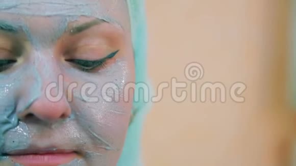 一个微笑的女人的脸头上有一条毛巾皮肤上有一刷蓝色的粘土看着镜头视频的预览图